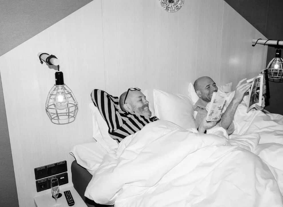 Two men in bed reading and smiling.